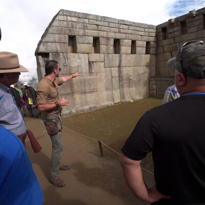 Timothy Alberino pointing out the ingenious anti-seismic architecture incorporated into the megalithic walls of the Main Temple at Machu Picchu, Peru.
